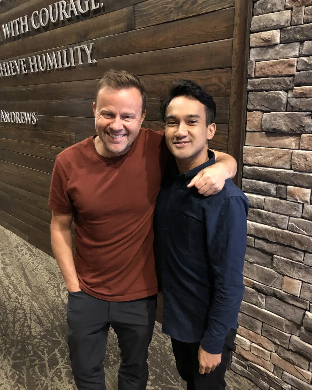 Daniel Lee standing arm in arm with a fellow singer in front of a wooden wall